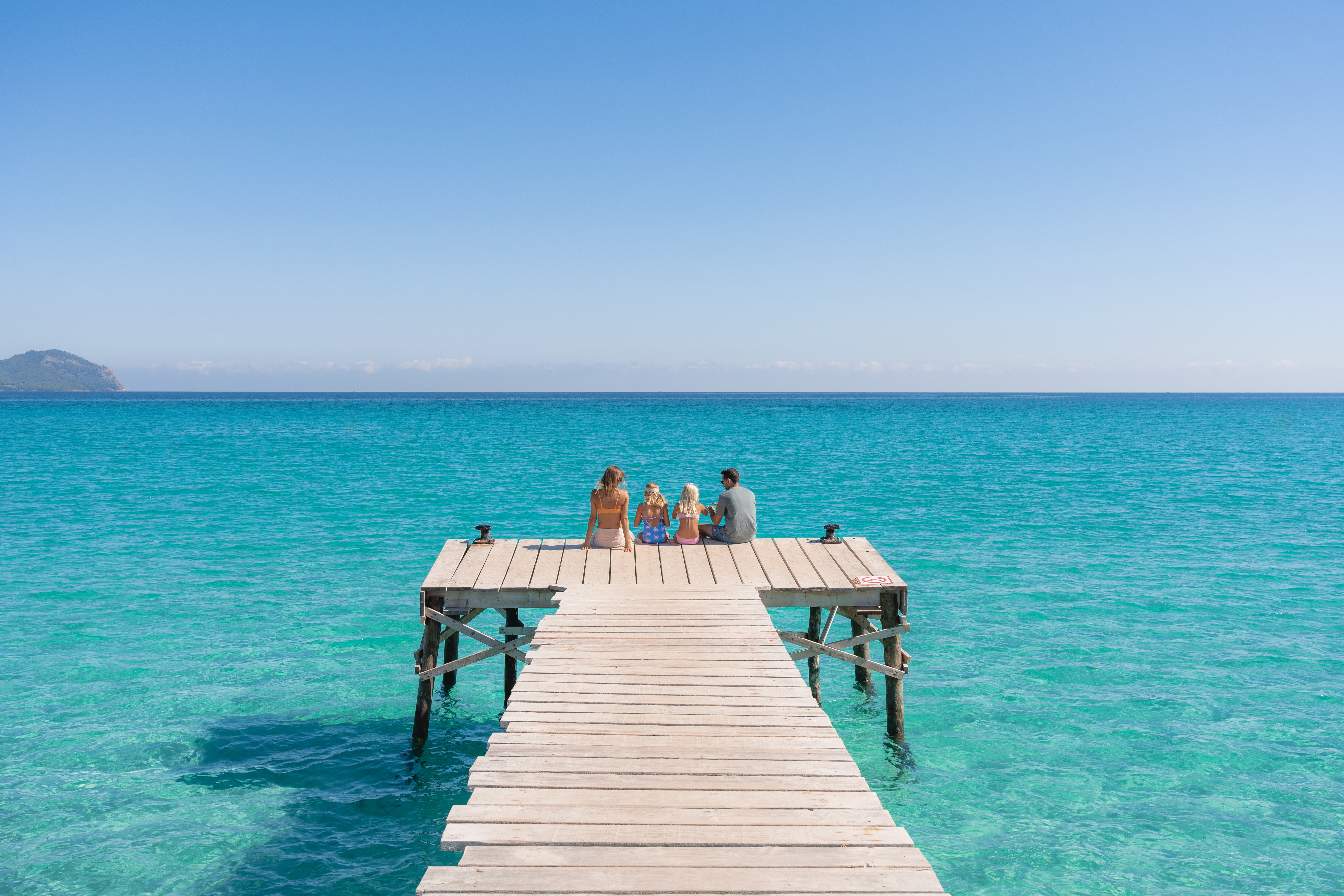 Family relaxing on wooden pier over turquoise sea