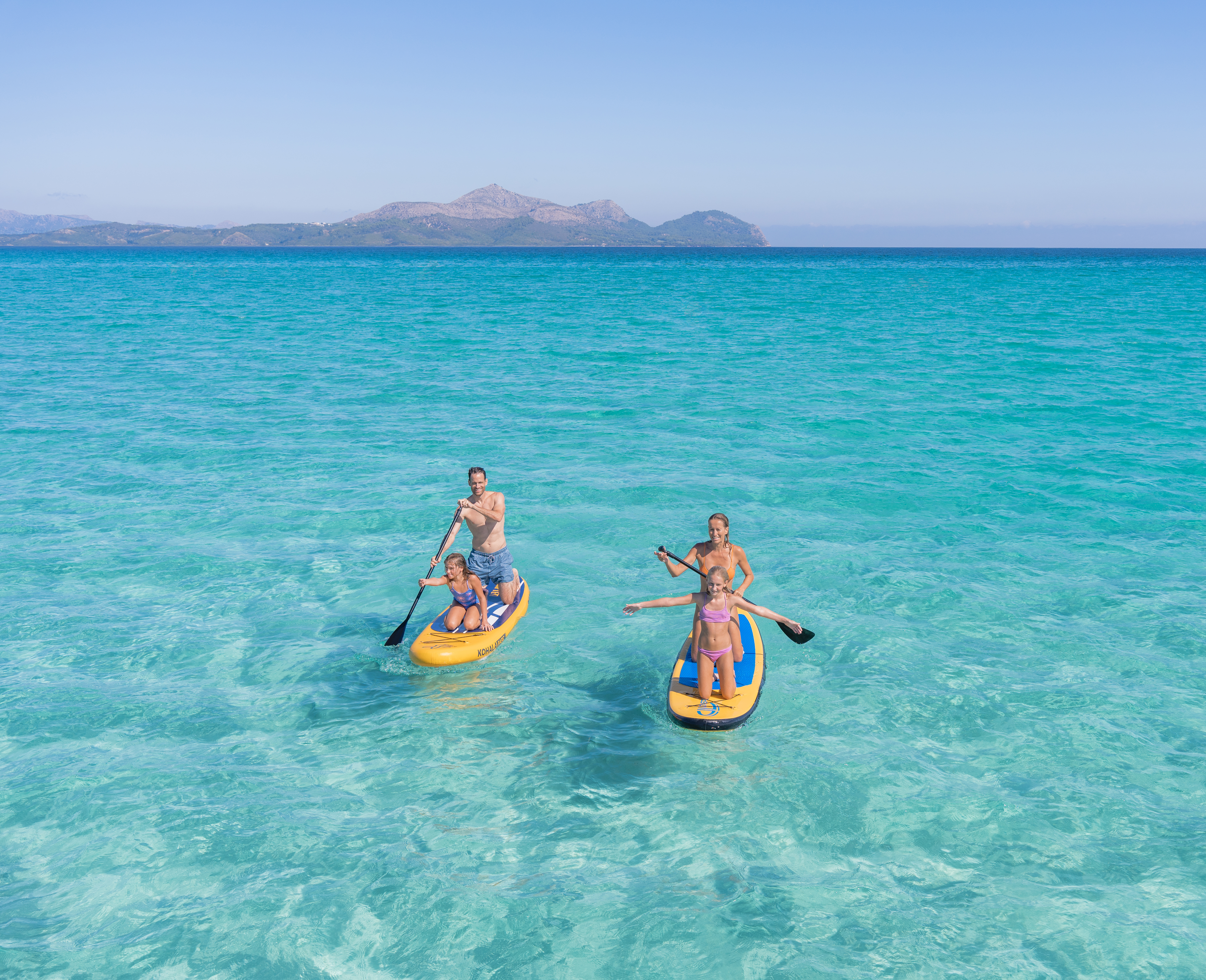 Family paddleboarding on clear turquoise sea
